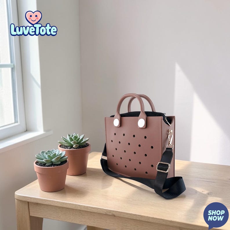 May include: A mauve tote bag with a black interior and a black shoulder strap. The bag has a series of circular perforations and two top handles. The logo "Luvetote" is in the upper left corner. Two small potted succulents are on the table.