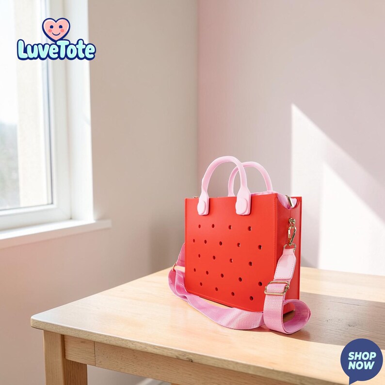 May include: A red tote bag with a perforated design, featuring pink handles and a matching shoulder strap. The bag has a gold-colored clasp and the text "Luvetote" is visible in the upper left corner. The bag is sitting on a wooden table.