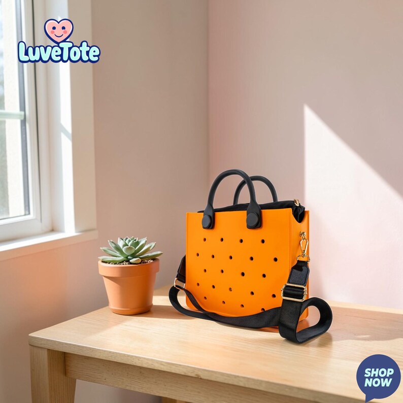 May include: Bright orange tote bag with black handles and a black shoulder strap. The bag has a series of small, evenly spaced black dots. A small potted succulent plant sits on a wooden table next to the bag. The Luvetote logo is in the upper left corner.