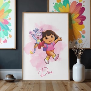 Könnte beinhalten: Gerahmter Druck mit Dora der Entdeckerin und Boots dem Affen, vor einem rosa Aquarellhintergrund. Dora trägt ein rosa Oberteil, orangefarbene Shorts und gelbe Schuhe. Der Druck enthält den Namen "Dora" in Kursivschrift.