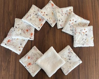 May include: A collection of square fabric coasters arranged in a circular pattern. The coasters feature a floral pattern with white, pink, and orange flowers on a light background. One coaster is plain white.