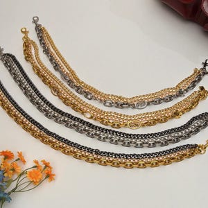 Puede incluir: Una variedad de correas de cadena decorativas para bolsos en oro, plata y negro. Cada correa presenta una combinación de diferentes estilos de cadena, incluyendo cadenas de eslabones y rolo. Diseñadas como accesorios elegantes para bolsos.