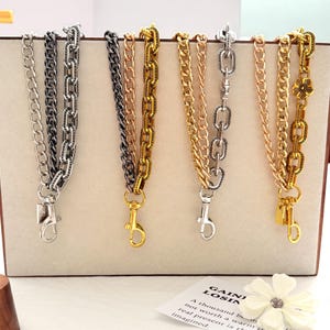 Puede incluir: Exhibición de varias correas de cadena metálicas para bolsos. Las cadenas son en tonos plateado, negro, dorado y oro rosa, con diferentes estilos de eslabones y cierres de mosquetón. Algunas cadenas tienen elementos decorativos.