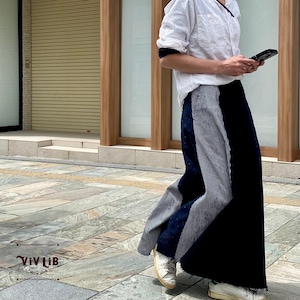 Peut inclure: Une jupe longue jusqu'au sol présentant un design color-block avec un panneau bleu marine foncé uni d'un côté et un motif à fines rayures verticales blanches et bleu marine de l'autre. La jupe est portée avec une chemise blanche.