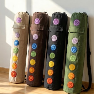May include: Four yoga mat bags in beige, brown, black, and olive green. Each bag features a pocket and embroidered chakra symbols in various colors. The bags have a drawstring closure and a black shoulder strap.