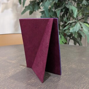 May include: A rectangular picture frame stand featuring a deep burgundy velvet-textured backing. The frame is positioned upright, showcasing the triangular support structure and the dark purple edge of the frame border visible from this side angle.