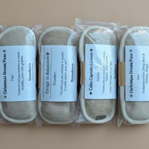 May include: Four packaged slippers with white labels. The labels have text that reads "Christmas Dream Pass", "Escape to Relaxation", and "Calm Captain License". The slippers are beige with a white border.