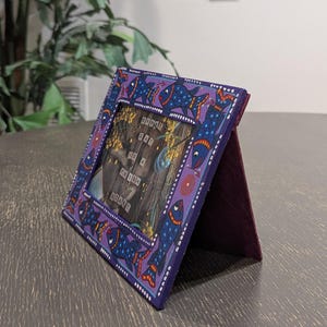 May include: A rectangular purple picture frame featuring a hand-painted pattern of blue fish with orange and white details. The frame contains a print with the text "EVERY DAY IS A FRESH START" displayed over a dark wood-grain background.