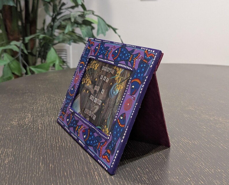 May include: A rectangular purple picture frame featuring a hand-painted pattern of blue fish with orange and white details. The frame contains a print with the text "EVERY DAY IS A FRESH START" displayed over a dark wood-grain background.
