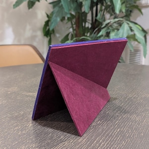 May include: A rectangular picture frame shown from the back, featuring a deep purple outer border and a dark maroon velvet-textured easel stand. The frame is angled to stand upright, displaying the structural support mechanism on its rear side.