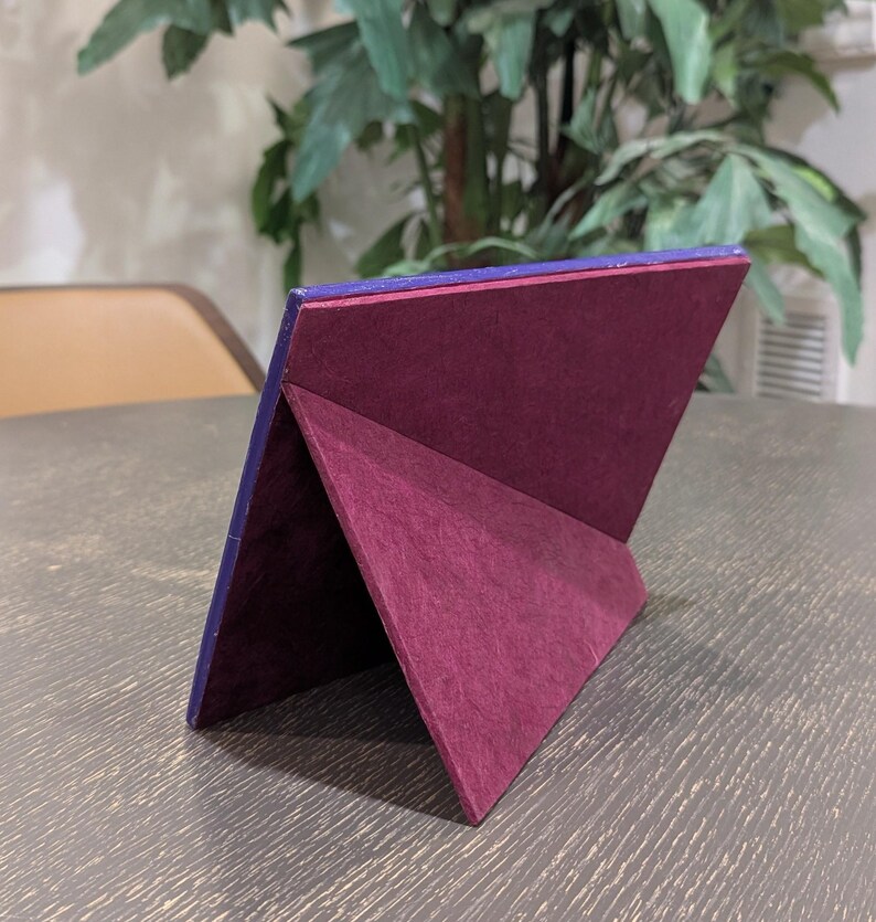 May include: A rectangular picture frame shown from the back, featuring a deep purple outer border and a dark maroon velvet-textured easel stand. The frame is angled to stand upright, displaying the structural support mechanism on its rear side.