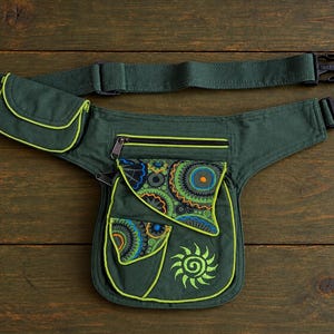 May include: A dark green canvas waist bag featuring a black plastic buckle, an adjustable strap, and multiple zippered compartments. The bag is accented with lime green piping and a sun-shaped embroidery, plus patterned fabric overlays.