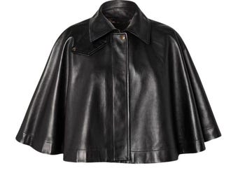 May include: A black leather cape with a collar and button closure. The cape has a smooth, shiny finish and a classic design. The garment is a stylish outerwear piece.
