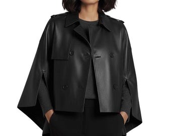 May include: A black leather cape jacket with a double-breasted front and a notched collar. The jacket has a classic design with button closures and a cape-like silhouette. The model is wearing a gray sweater and black pants.