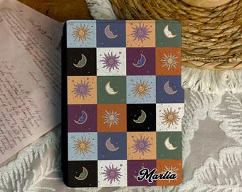 May include: A patterned notebook with a patchwork design of suns and crescent moons in different colours. The notebook has the name "Marlia" in a cursive font. The cover is black.