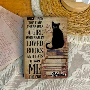 May include: A rectangular book cover with the text "ONCE UPON THE TIME THERE WAS A GIRL WHO REALLY LOVED BOOKS AND CATS IT WAS ME THE END" and a black cat illustration. The cat sits atop a stack of books. The name "Marlia" is written at the bottom.