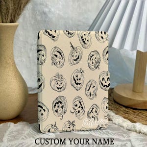 Może przedstawiać: Beżowe etui na tablet z powtarzającym się wzorem czarnych, liniowych dyni. Etui ma zaokrąglone rogi i tekst "CUSTOM YOUR NAME" na dole. W tle dekoracyjny wazon i lampa.