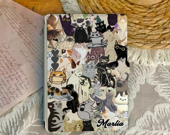 May include: A cream-colored tablet case featuring a collage of various cat illustrations in different poses and colors. The name "Marlia" is written in cursive at the bottom right corner. The case is designed to protect a tablet.