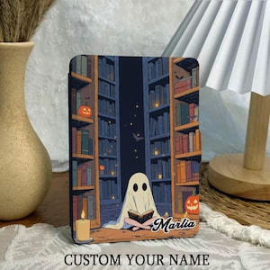May include: A decorative tablet case featuring a whimsical illustration of a ghost reading in a library, with pumpkins and a candle. The case has the text "CUSTOM YOUR NAME" at the bottom and the name "Marlia" on the right side.