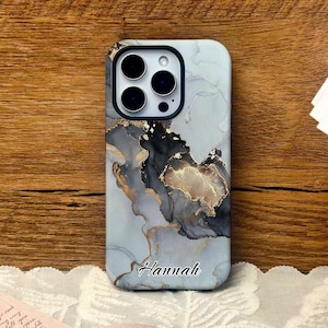 May include: A light blue phone case with a marble design in shades of gray, black, and gold. The name "Hannah" is written in cursive at the bottom. The case has a camera cutout and a black border.