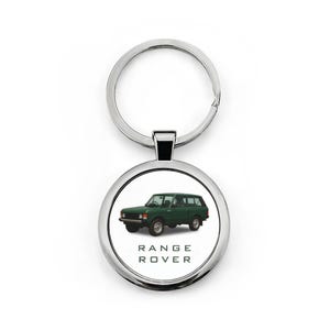 Könnte beinhalten: Ein silberner Schlüsselanhänger mit einem runden Anhänger, der einen grünen Range Rover SUV zeigt. Der Text "RANGE ROVER" ist in Schwarz unter dem Fahrzeugbild gedruckt. Der Schlüsselanhänger hat einen geteilten Ring zum Befestigen von Schlüsseln.