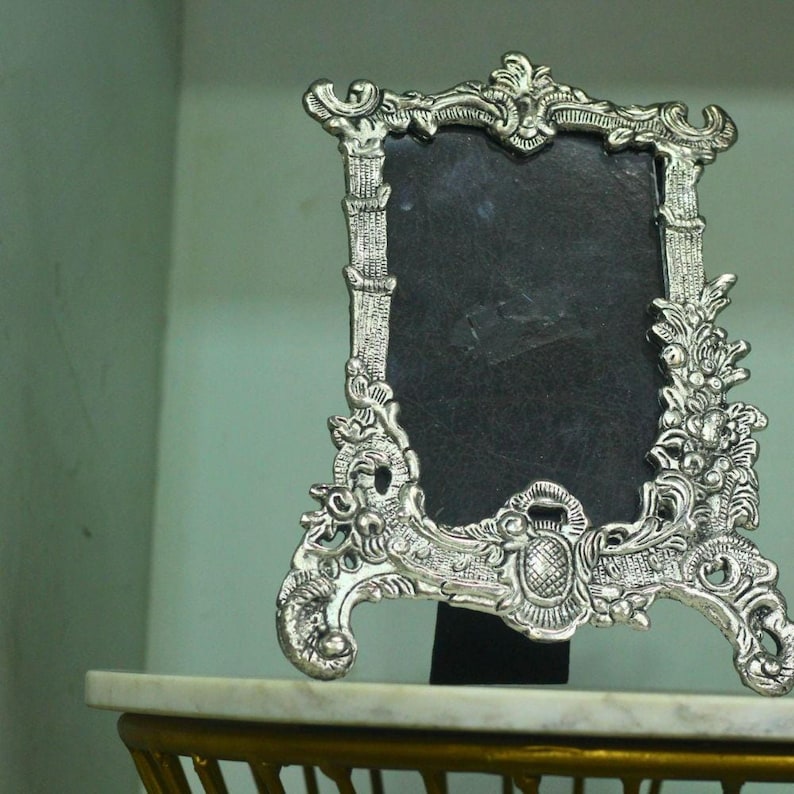 Vintage silver baroque-style picture frame with ornate floral scrollwork and an empty dark center on a tabletop.