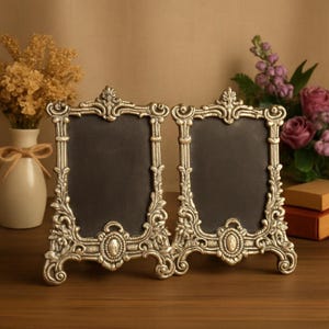 Vintage silver baroque-style picture frame with ornate floral scrollwork and an empty dark center on a tabletop.