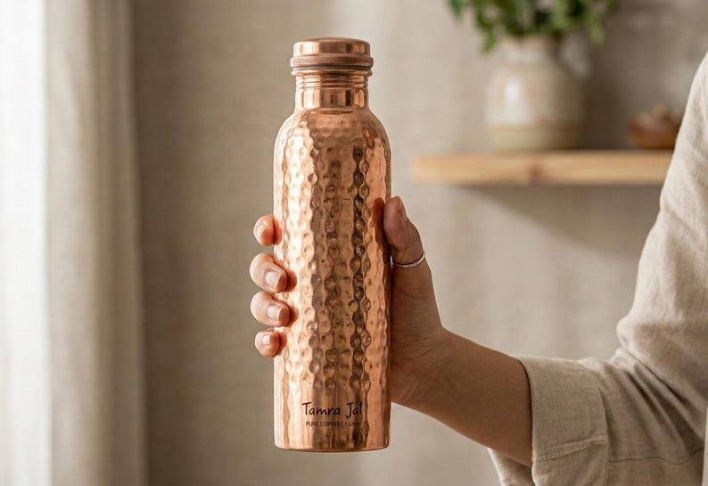 Pure copper water bottle hammered with a dimpled finish and copper cap, held; reusable hydration bottle, copper vessel.