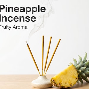 Może przedstawiać: Obrazek patyczków do kadzidła o zapachu ananasa z napisem "Pineapple Incense Fruity Aroma". Patyczki do kadzidła znajdują się w małym białym wazonie, z kawałkiem ananasa i jego zielonymi liśćmi po prawej stronie. Dym unosi się z zapalonego kadzidła.