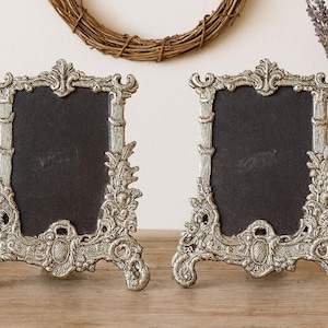 Pair of silver Baroque-style ornate picture frames, a frame set, with black centers on a wooden tabletop.