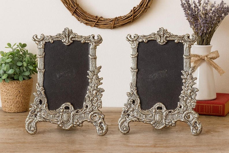 Pair of silver Baroque-style ornate picture frames, a frame set, with black centers on a wooden tabletop.