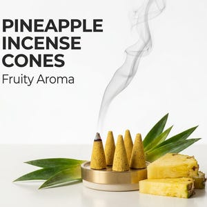 Może przedstawiać: Zdjęcie stożków kadzidła ananasowego z napisem "PINEAPPLE INCENSE CONES Fruity Aroma". Stożki są żółte i znajdują się w złotym i białym uchwycie. Dym unosi się z jednego stożka, a także obecne są plastry i liście ananasa.