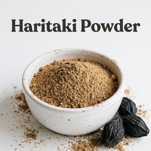 May include: A white ceramic bowl filled with brown Haritaki powder, with a few dark, dried Haritaki fruits next to it. The words "Haritaki Powder" are printed in black above the bowl.