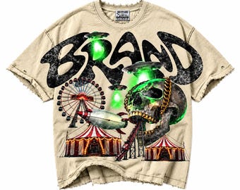 Puede incluir: Una camiseta beige de manga corta con bordes desgastados que presenta un gran gráfico negro con la palabra BRAND. El diseño incluye una calavera con una cadena dorada, una noria, carpas de circo, un cohete y ovnis verdes brillantes.