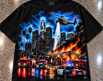 May include: A black short-sleeve t-shirt featuring a graphic print of a city skyline at night with a helicopter spraying water on a burning gas station. Fire trucks and police cars with flashing lights are parked in the foreground.