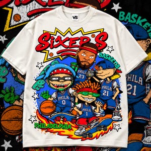 Puede incluir: Una camiseta de manga corta color crema con un estampado gr&aacute;fico de personajes de dibujos animados con camisetas de baloncesto azules de Filadelfia. El dise&ntilde;o incluye el texto "SIXER'S" en rojo, "PHILADELPHIA" y "BASKETBALL" en verde, con balones y estrellas.