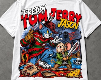 Puede incluir: Una camiseta blanca con un estampado gráfico de un gato vestido como Freddy Krueger y un ratón con máscara de hockey como Jason Voorhees. El texto dice "FREDDY VS JASON" y "TOM JERRY". La escena incluye una ratonera, queso y una calavera.