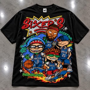 Puede incluir: Una camiseta negra de manga corta con un gran estampado gr&aacute;fico con el texto SIXER'S y PHILADELPHIA. El dise&ntilde;o muestra cuatro personajes de dibujos animados con camisetas de baloncesto azules con los n&uacute;meros 0, 1, 21 y 23, junto a un bal&oacute;n.