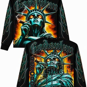 Op de afbeelding: Een zwart sweatshirt met lange mouwen en een afbeelding van het Vrijheidsbeeld dat een sigaar rookt tegen een vurige achtergrond. De tekst "Godsplan" staat bovenaan, terwijl de achterkant "REAL NEVER DIES" en "RECORDS WORLD.TOUR" toont.