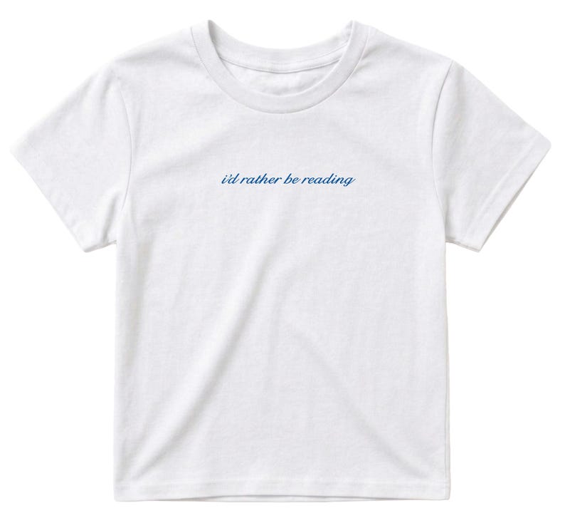 May include: White t-shirt with a crew neck and short sleeves. The text "i'd rather be reading" is printed in a cursive blue font across the chest. The shirt is made of a soft, lightweight material.