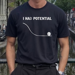 May include: Black t-shirt with the white text "I HAD POTENTIAL" above a white line and a white ball graphic. The shirt is a crew neck and is being worn by a person.
