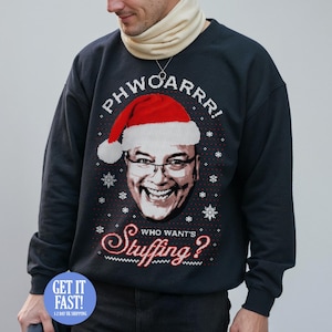 May include: Dark navy sweatshirt featuring a graphic of a man in a Santa hat and glasses. The text says "PHWOARRR!" above the image and "Who wants Stuffing?" below. Snowflake designs are also included.