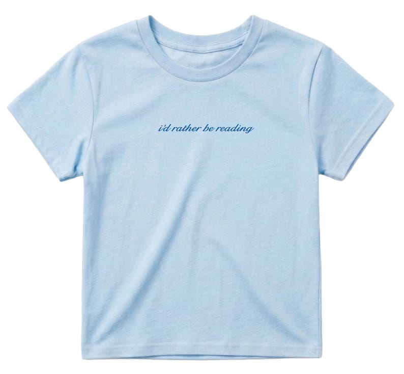 May include: A light blue t-shirt with the phrase "i'd rather be reading" in a cursive font. The shirt has short sleeves and a crew neck. The fabric appears to be soft and lightweight, suitable for casual wear.