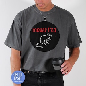 May include: Charcoal grey t-shirt with a circular design displaying the words "mouse rat" in red and a white rat outline. The shirt is paired with black jeans and a silver necklace. A black travel mug is held.