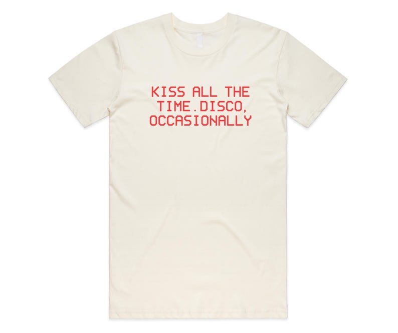 May include: Cream-colored t-shirt with the red text "KISS ALL THE TIME. DISCO, OCCASIONALLY" printed across the front. The shirt has short sleeves and a crew neck.