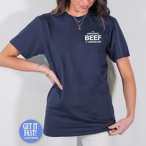 May include: Navy blue t-shirt featuring the text "THE ORIGINAL BEEF of CHICAGOLAND". The shirt has a crew neck and short sleeves.