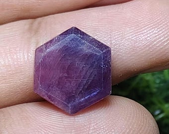 Op de afbeelding: Een gefacetteerde, zeshoekige edelsteen met een diepe paarse kleur. Het oppervlak van de edelsteen reflecteert licht en toont zijn kristalstructuur. De steen wordt in een hand gehouden, wat de grootte en vorm benadrukt. Geschikt voor sieraden maken of verzamelen.