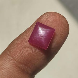 Könnte beinhalten: Ein kleiner, quadratischer Edelstein in leuchtendem Magentarosa mit einer glatten, polierten Oberfläche. Der Stein hat eine flache Oberseite und gerade Kanten und zeigt einen gleichmäßigen, gesättigten Farbton in seiner gesamten kristallinen Struktur.