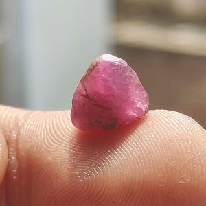 以下が含まれることがあります： 鮮やかで半透明な濃いピンクからマゼンタの色合いをした、小さく未加工の研磨されていない宝石。この石は不規則で角張った形状をしており、結晶構造全体に自然なファセットと内部のインクルージョンが見られます。