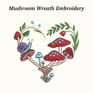 May include: Embroidered heart-shaped design featuring red mushrooms with blue spots, a purple snail, and green leaves. The text "Mushroom Wreath Embroidery" is at the top. The design is on a cream-colored background.
